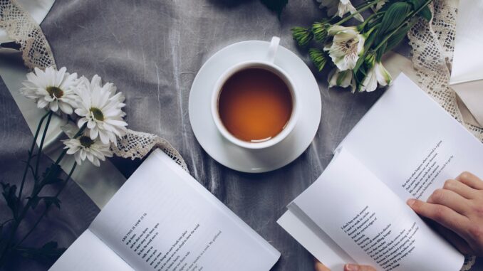 Inviting cozy reading setup with tea, poetry books, and fresh flowers on a table.