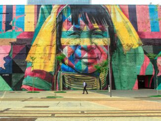 Colorful mural depicting a native face on an urban street wall with a passerby.