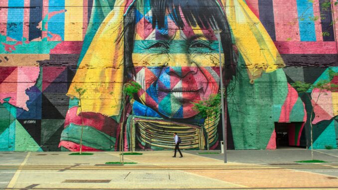 Colorful mural depicting a native face on an urban street wall with a passerby.