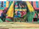 Colorful mural depicting a native face on an urban street wall with a passerby.