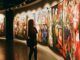 A woman observes vibrant paintings in an art gallery exhibition.