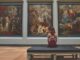 A woman observes classic paintings in an elegant museum gallery.