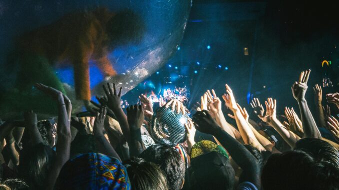 Lively concert scene with excited crowd and performer in a transparent ball at night.