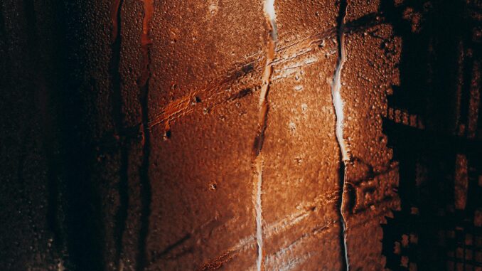 Water drops flowing on misted glass window during rain in cold dark evening
