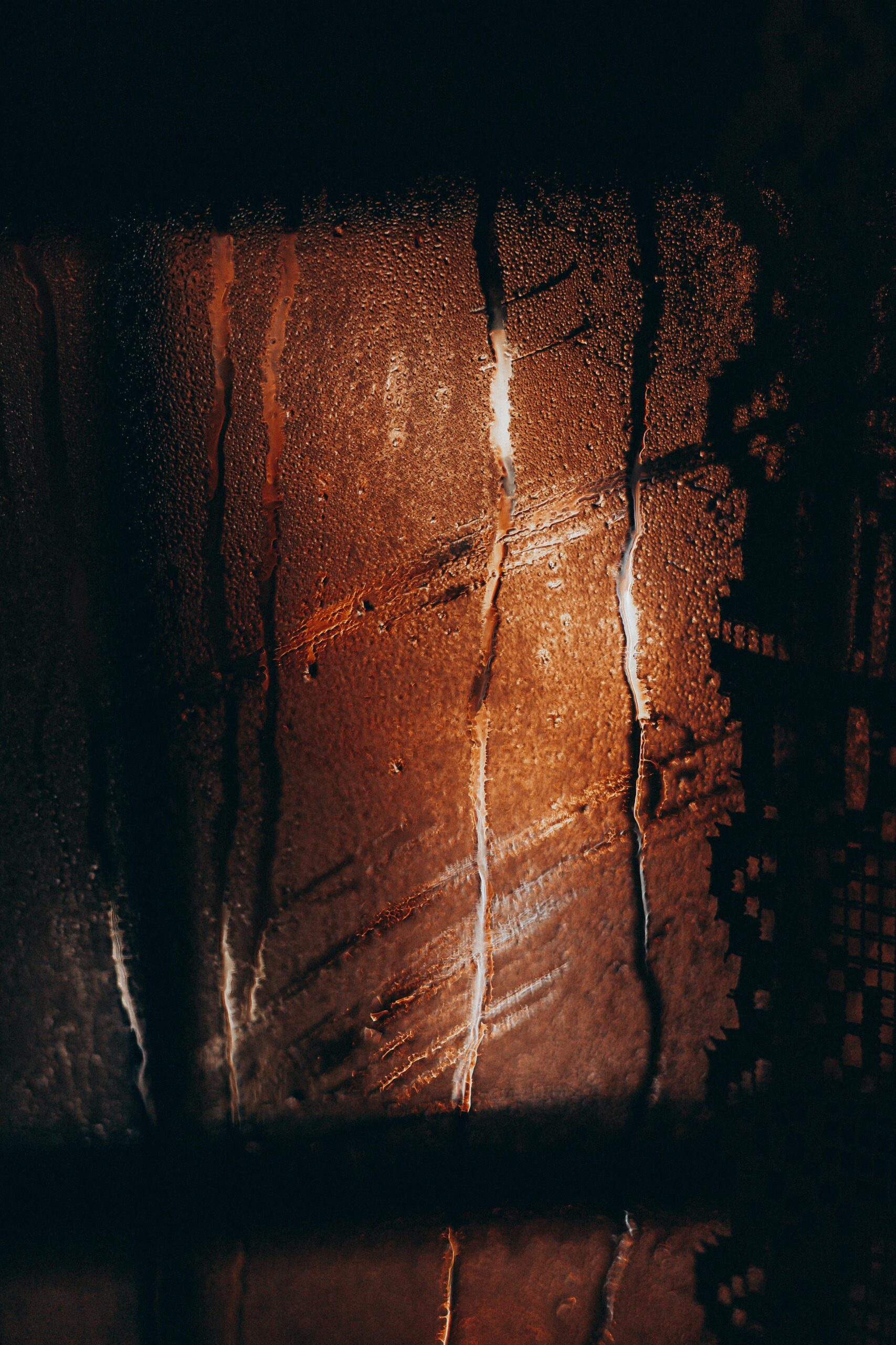 Water drops flowing on misted glass window during rain in cold dark evening