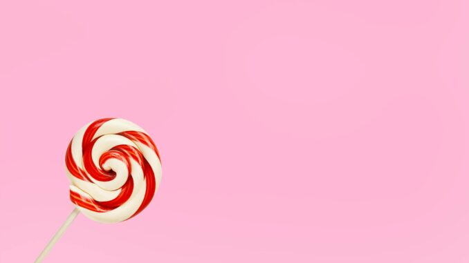 Vibrant red and white lollipop on a pastel pink background, perfect for confectionery themes.