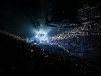 Energetic concert scene featuring a packed audience, vibrant lights, and a live performance on stage.