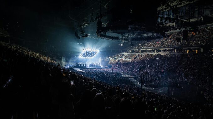 Energetic concert scene featuring a packed audience, vibrant lights, and a live performance on stage.