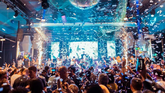 Vibrant nightclub scene in Mantua, Italy, featuring a lively crowd, confetti, and colorful lights.