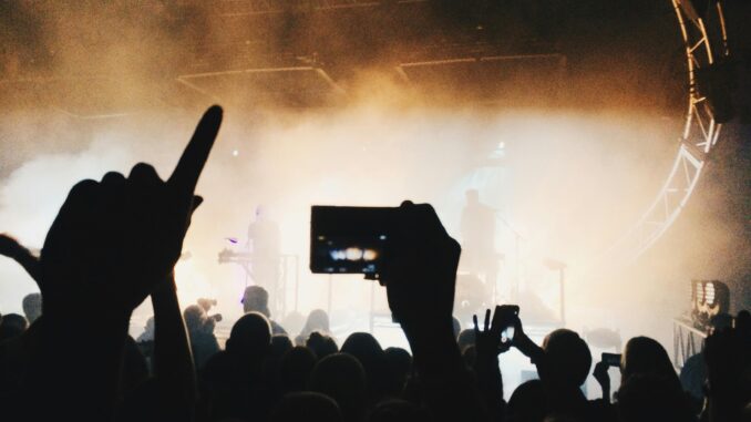 A vibrant concert scene with silhouettes of an energetic crowd capturing the moment on mobile phones.