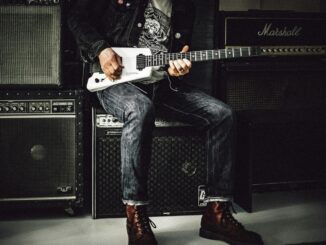 A musician plays an electric guitar in a studio, surrounded by amplifiers, showcasing rock and punk vibes.