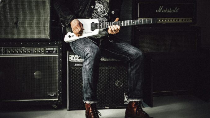 A musician plays an electric guitar in a studio, surrounded by amplifiers, showcasing rock and punk vibes.