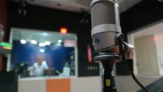 Close-up of a microphone in a recording studio with a blurred sound engineer in the background.