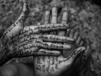 Artistic black and white photo of hands with handwritten text on skin.