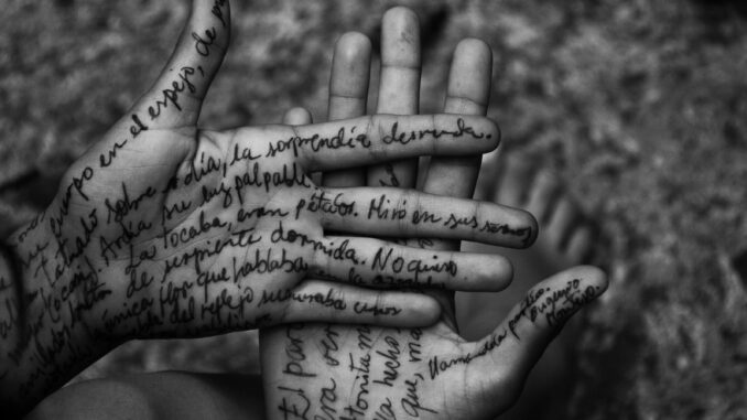 Artistic black and white photo of hands with handwritten text on skin.