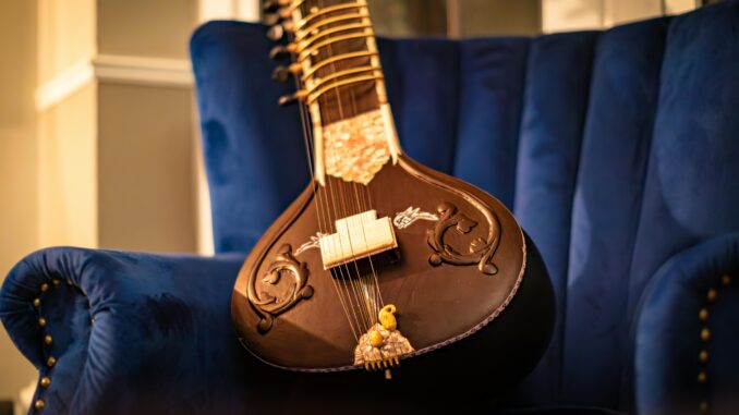 A beautifully crafted sitar resting on a plush blue velvet chair in a cozy room.