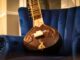 A beautifully crafted sitar resting on a plush blue velvet chair in a cozy room.