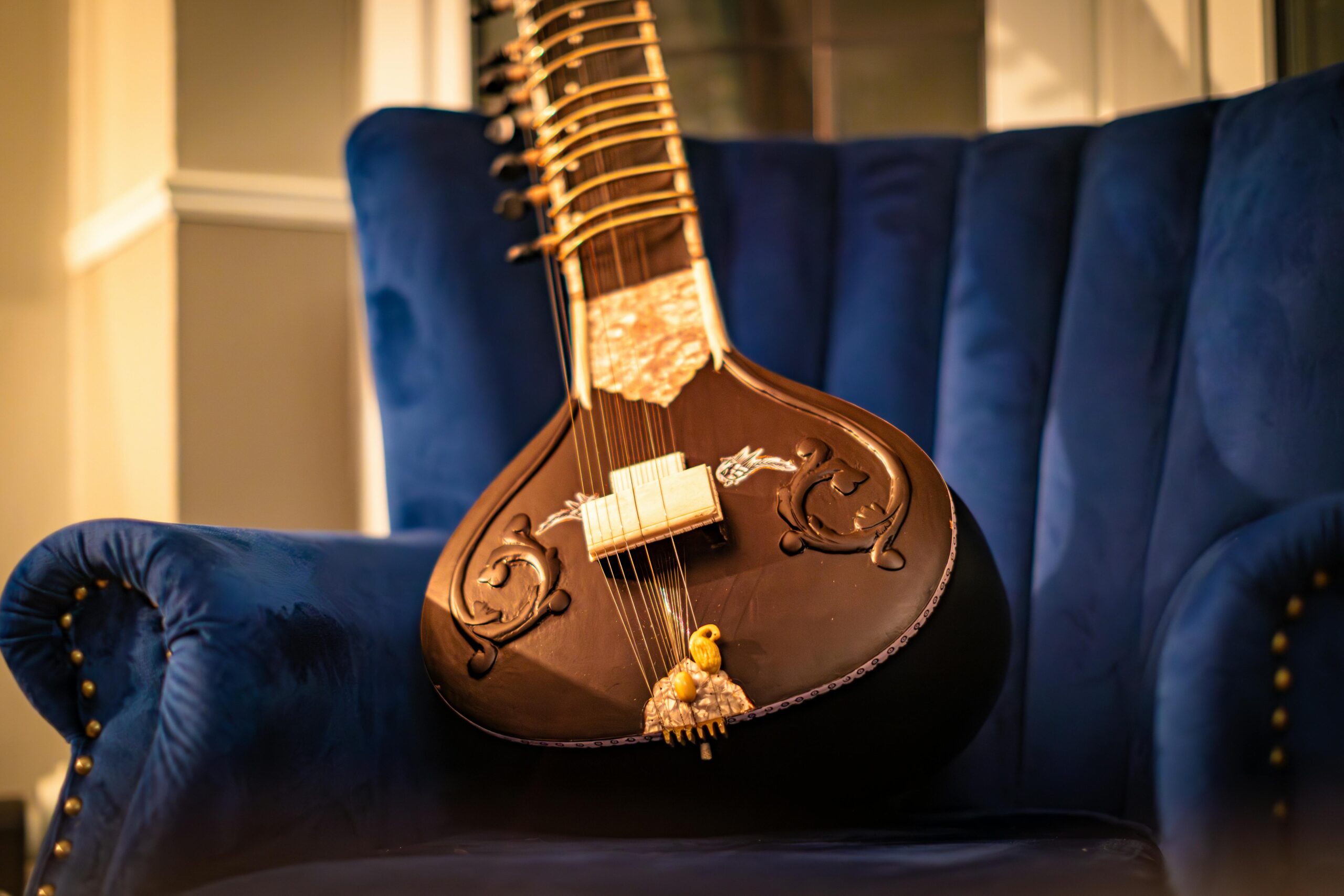 A beautifully crafted sitar resting on a plush blue velvet chair in a cozy room.