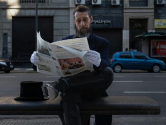A stylish man in formal attire reads a newspaper on a bench in Buenos Aires.