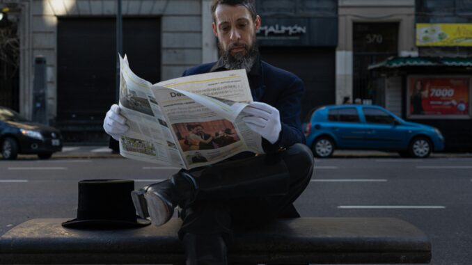 A stylish man in formal attire reads a newspaper on a bench in Buenos Aires.