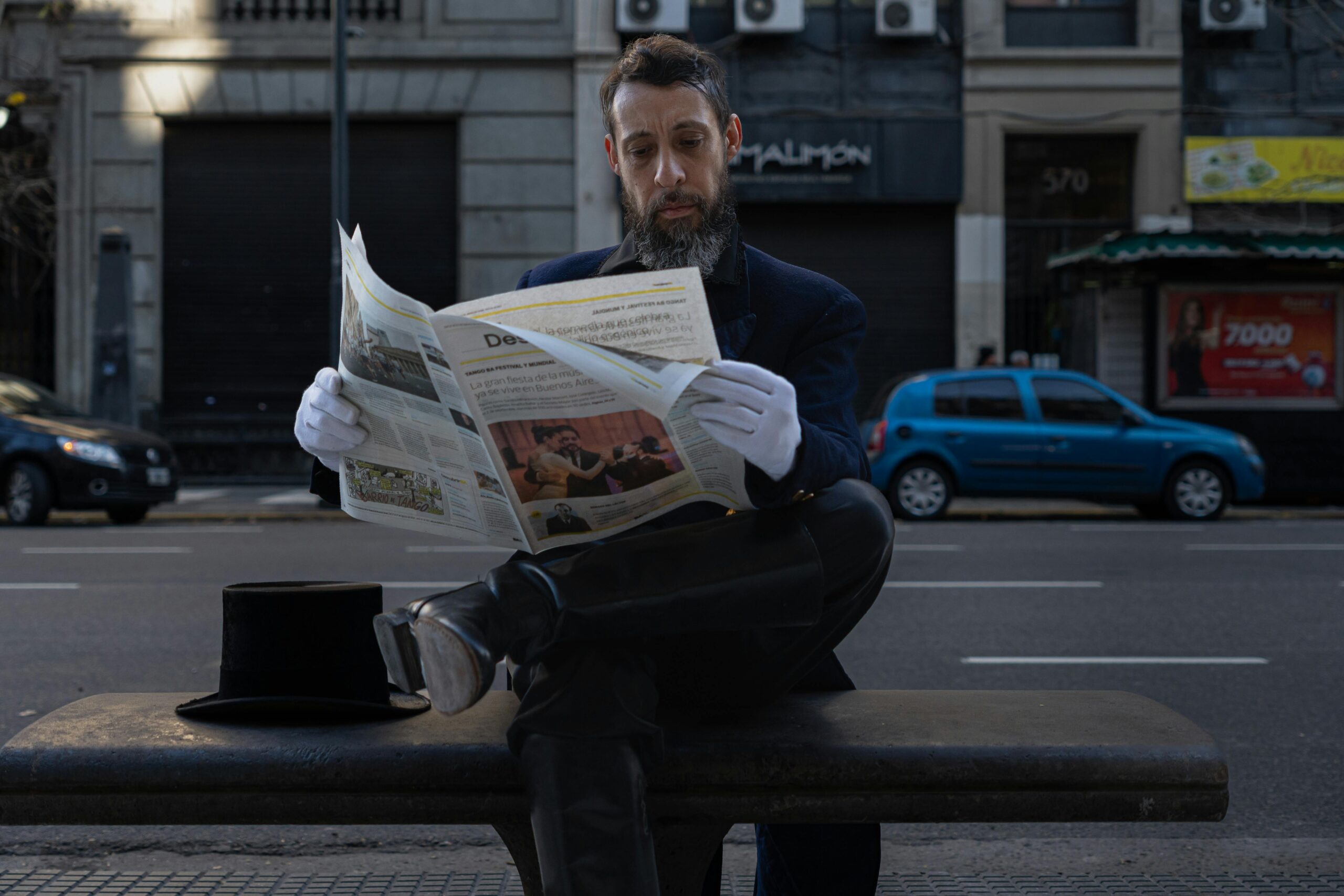 A stylish man in formal attire reads a newspaper on a bench in Buenos Aires.