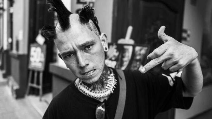 Black and white street portrait of a punk enthusiast with unique hairstyle and tattoos.