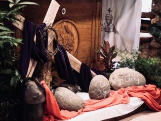 Indoor Easter display featuring a cross, draped cloth, and rocks with inscriptions, creating a spiritual ambiance.