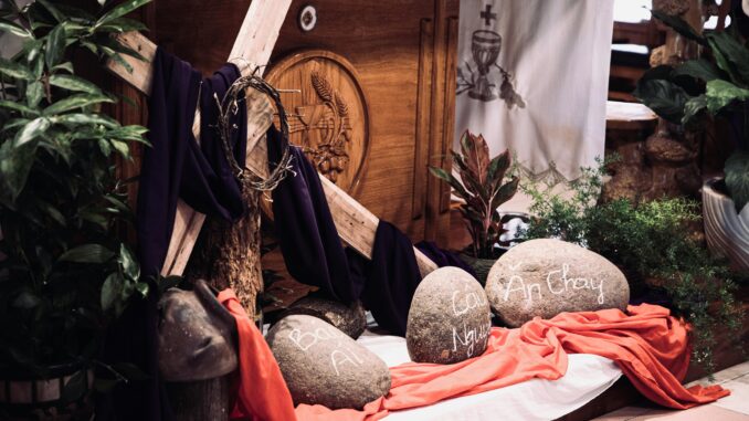 Indoor Easter display featuring a cross, draped cloth, and rocks with inscriptions, creating a spiritual ambiance.