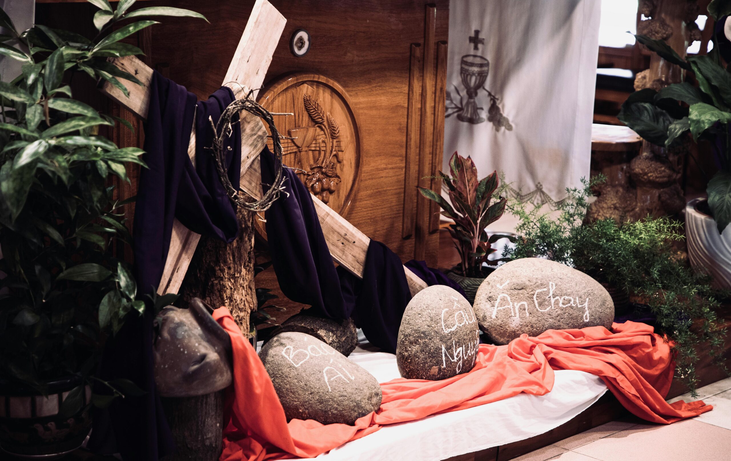 Indoor Easter display featuring a cross, draped cloth, and rocks with inscriptions, creating a spiritual ambiance.