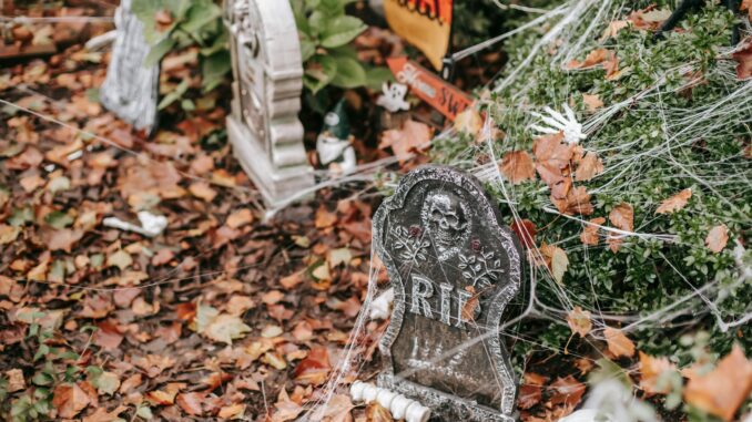 Fake graves covered in web with bones lying around near signs trick or treat and home sweet home on Halloween in autumn day