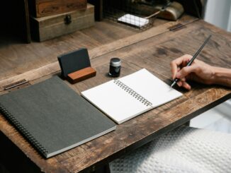 A close-up of a hand writing in a notebook at a tidy wooden desk, evoking creativity.
