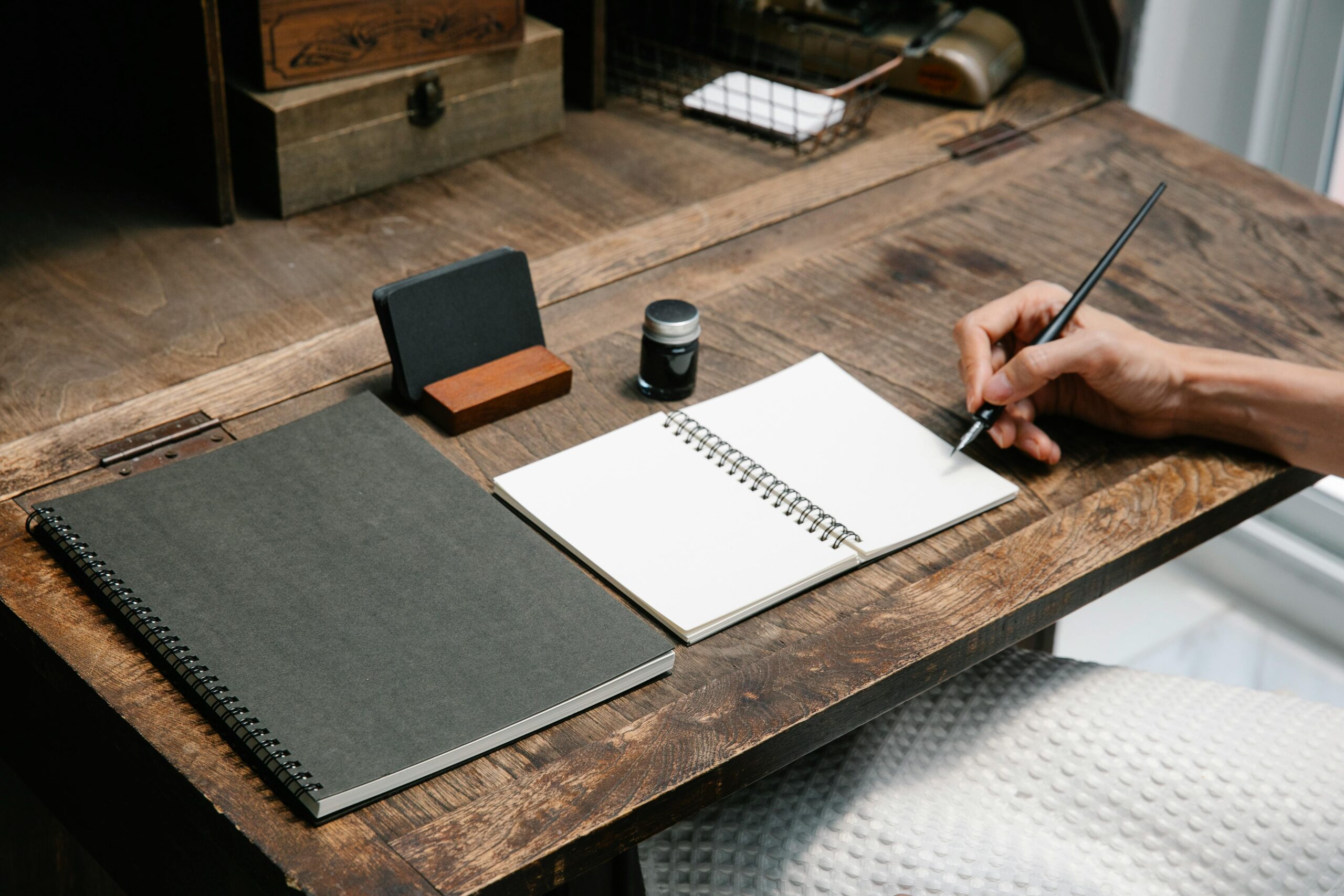 A close-up of a hand writing in a notebook at a tidy wooden desk, evoking creativity.