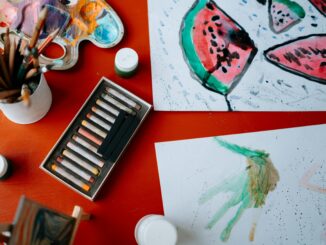 Creative art setup featuring watercolors and pastels on a red table, showcasing artistic expression.