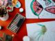 Creative art setup featuring watercolors and pastels on a red table, showcasing artistic expression.