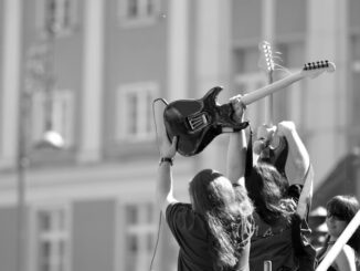 Dynamic black and white photo of musicians with guitars at an outdoor concert.