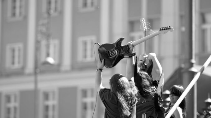 Dynamic black and white photo of musicians with guitars at an outdoor concert.