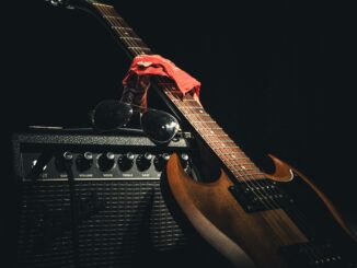Styled electric guitar resting on amplifier with sunglasses and scarf, capturing rock vibe.