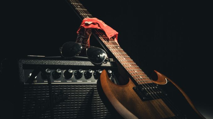 Styled electric guitar resting on amplifier with sunglasses and scarf, capturing rock vibe.