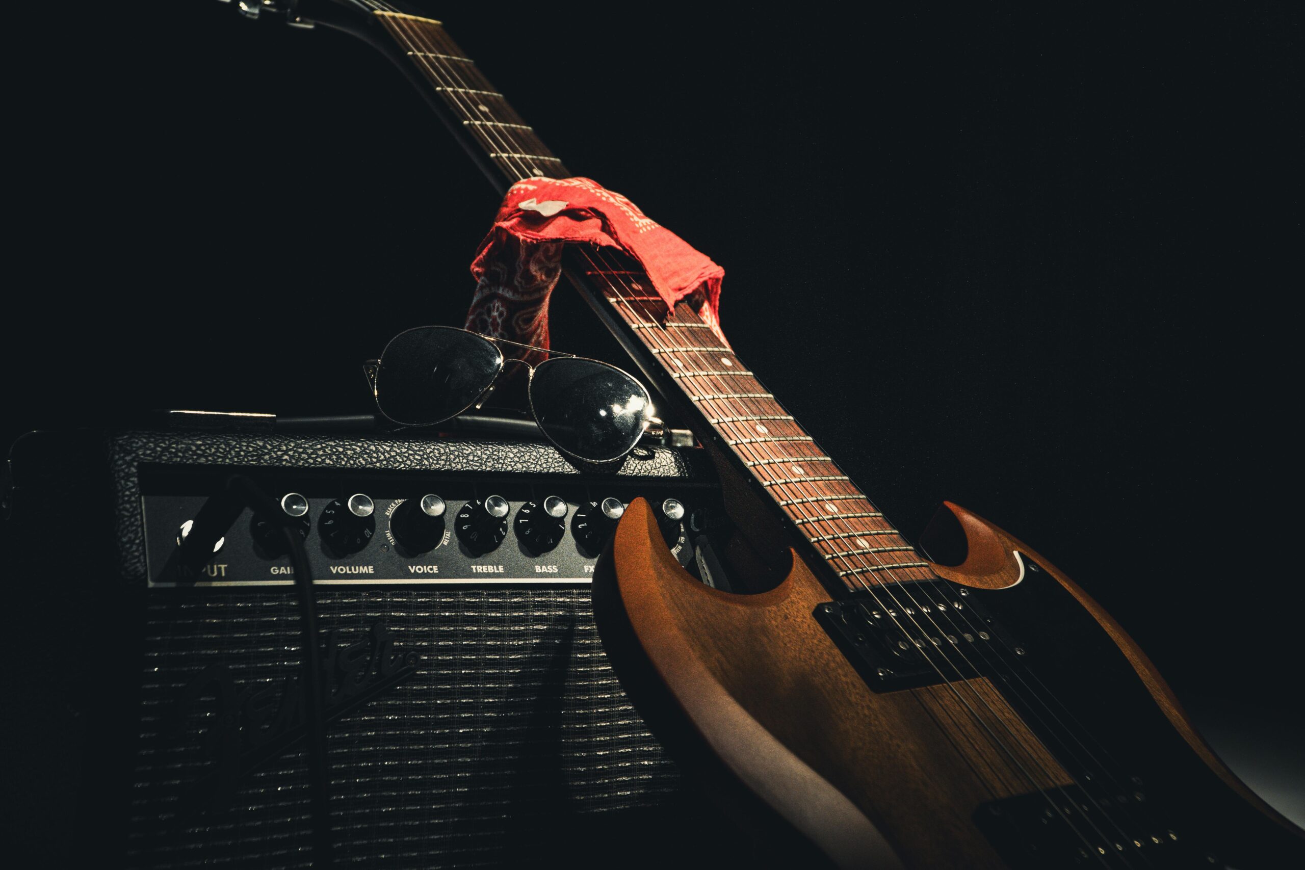 Styled electric guitar resting on amplifier with sunglasses and scarf, capturing rock vibe.