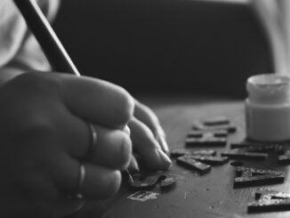 Black and white photo of hand crafting with wooden letters and paint.