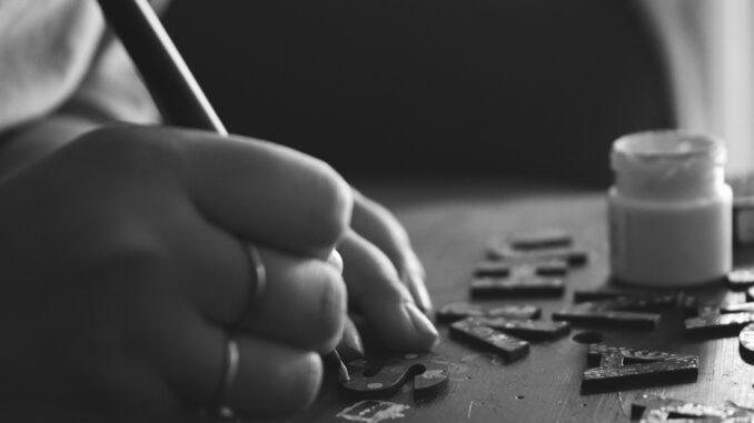 Black and white photo of hand crafting with wooden letters and paint.