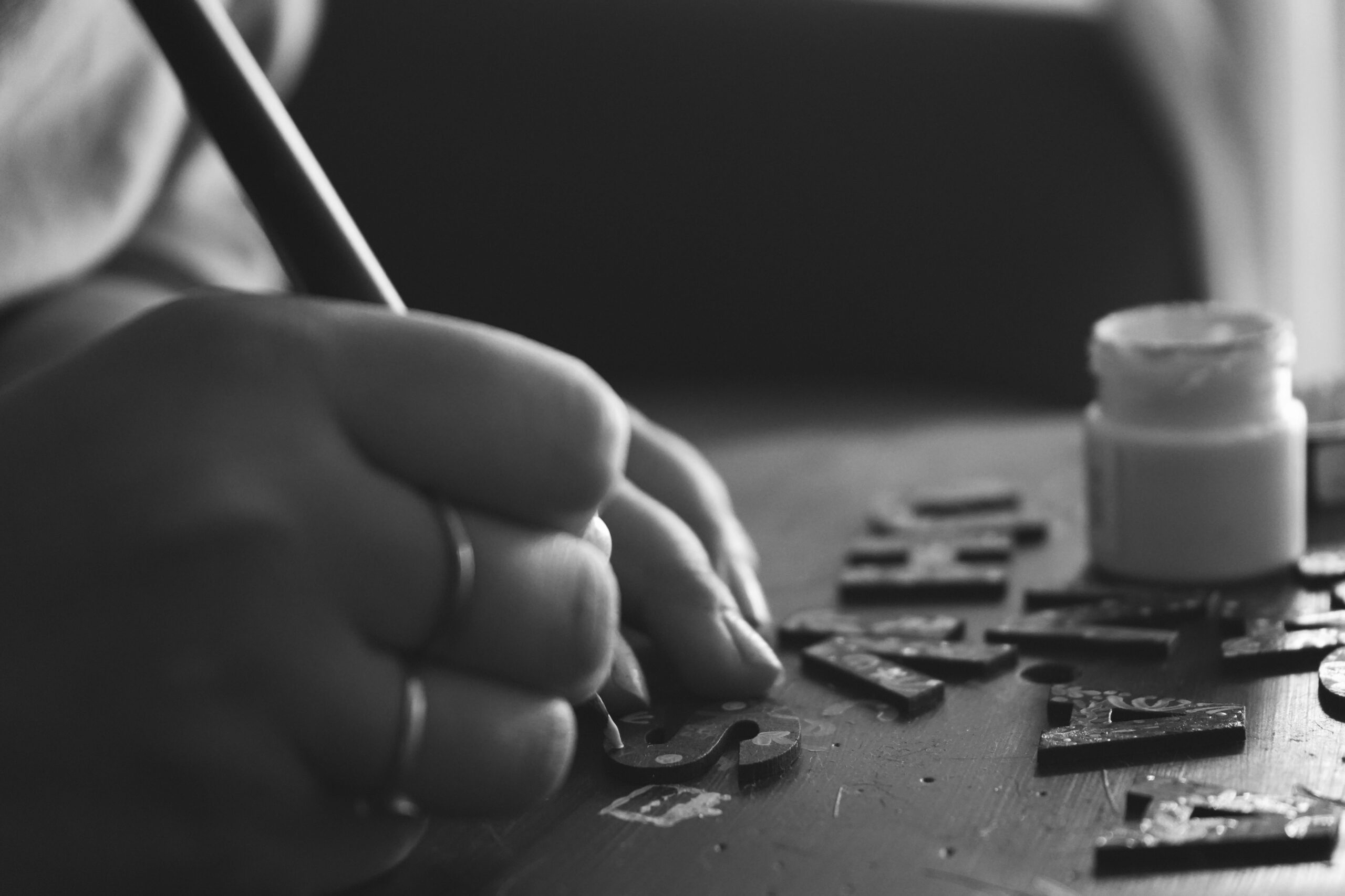 Black and white photo of hand crafting with wooden letters and paint.
