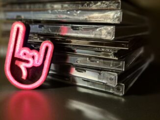 A vibrant rock hand symbol next to a stack of compact discs, reflecting music culture.
