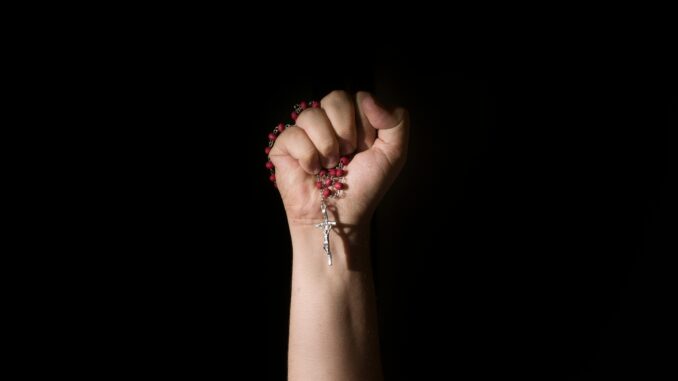 A close-up of a hand holding rosary beads with a cross in dramatic lighting.
