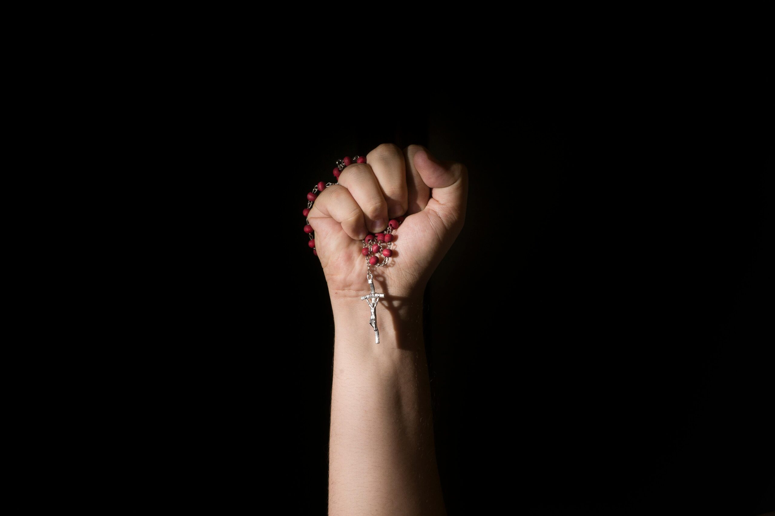 A close-up of a hand holding rosary beads with a cross in dramatic lighting.