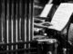 Monochrome image of a hand reaching for sheet music in a percussion setup.