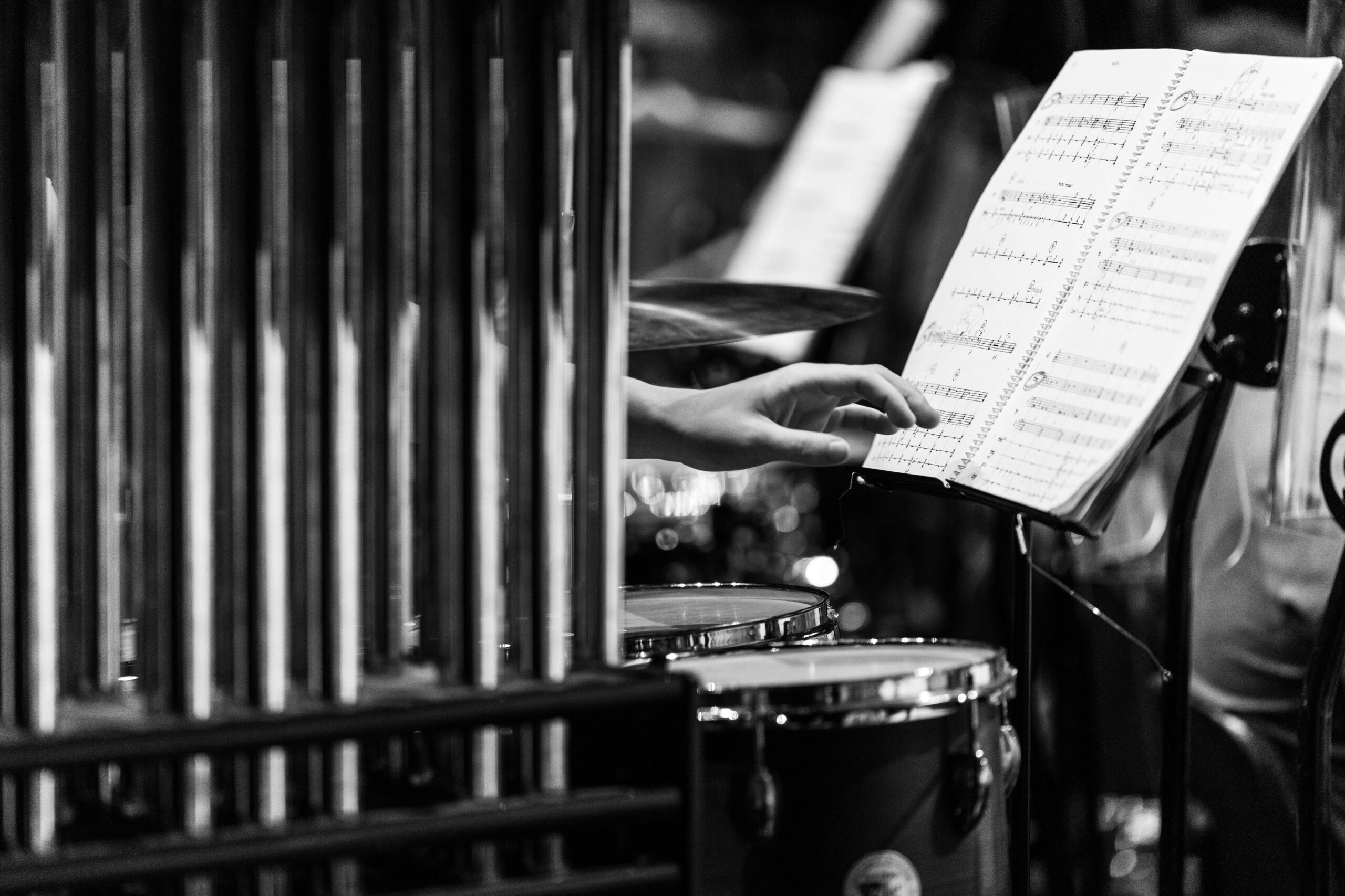 Monochrome image of a hand reaching for sheet music in a percussion setup.