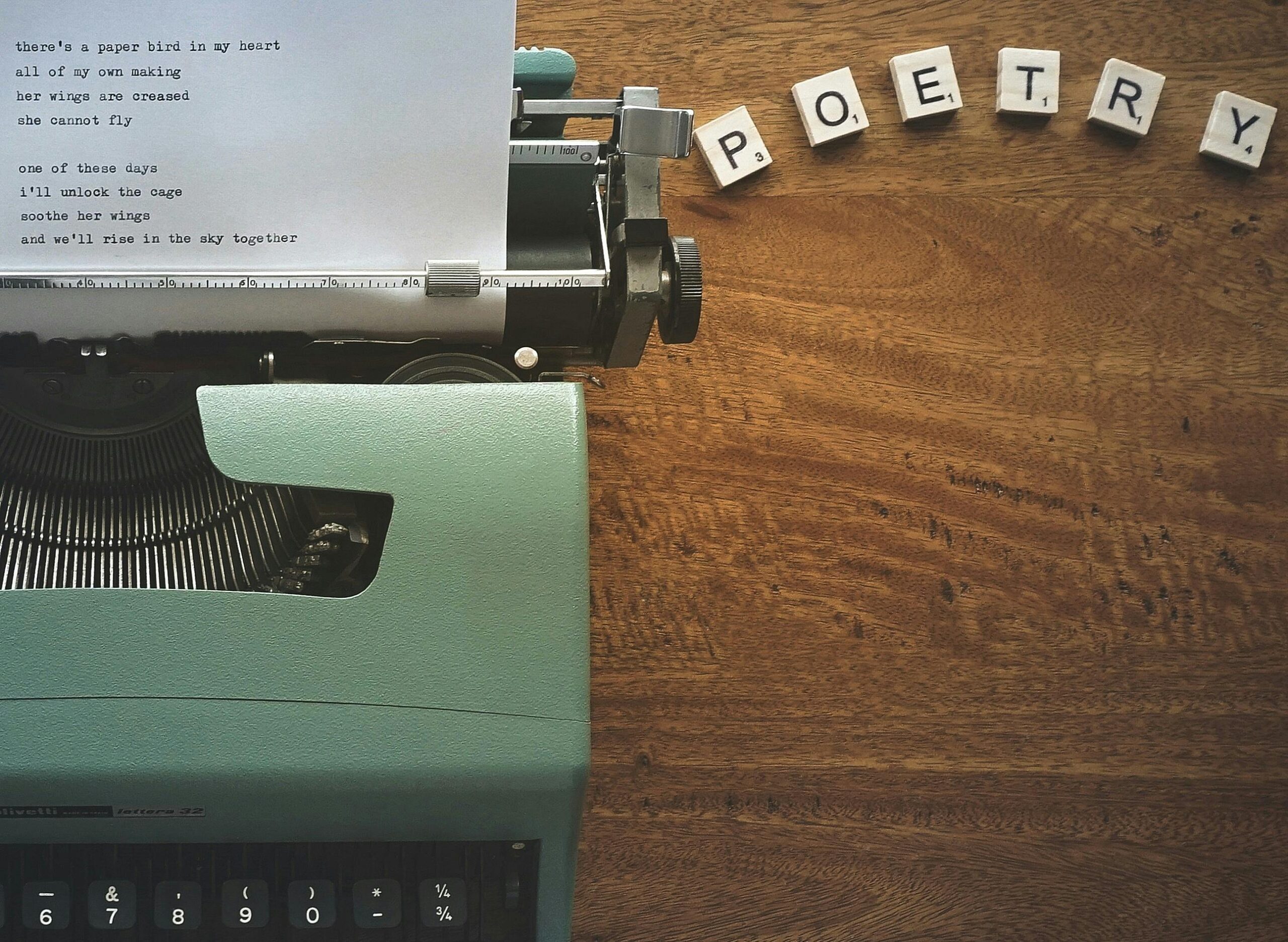 A typewriter creates poetic lines on paper amidst Scrabble tiles spelling 'POETRY'.