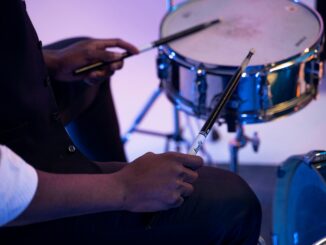 A musician playing a snare drum with drumsticks in a studio setting. Close-up view.