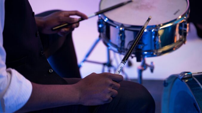 A musician playing a snare drum with drumsticks in a studio setting. Close-up view.